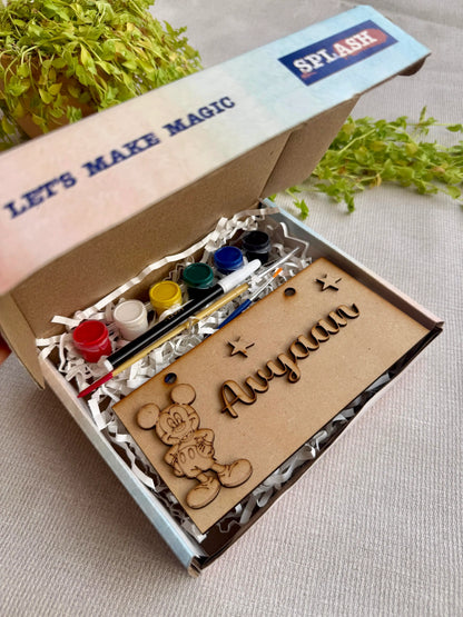 A personalized kids craft kit in a cardboard box, featuring wooden name cutouts, a Mickey Mouse design, acrylic paint bottles, and a paintbrush, with 'SPLASH' branding on the box lid.