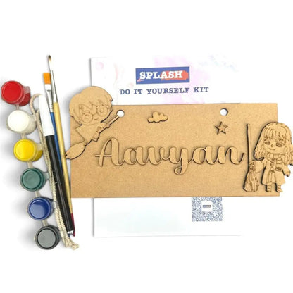 A DIY wooden name painting kit for kids, featuring a personalized wooden plaque with a cutout name 'Aavyan', cartoon girl and boy designs, a paint palette with six paint wells, and two paintbrushes on a white background.
