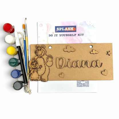 A DIY laser-engraving kit for personalized wooden signs, featuring a pre-cut wooden bear and child design, a wooden nameplate reading 'Diana', paint pots in various colors, and two paintbrushes on a white background.