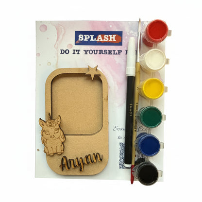 Personalized kids' DIY paint by numbers kit by Splash, featuring a wooden nameplate with a cartoon cat design and the name 'Anyan', a paint palette with six color wells, a paintbrush, and a paint pen on a white background.
