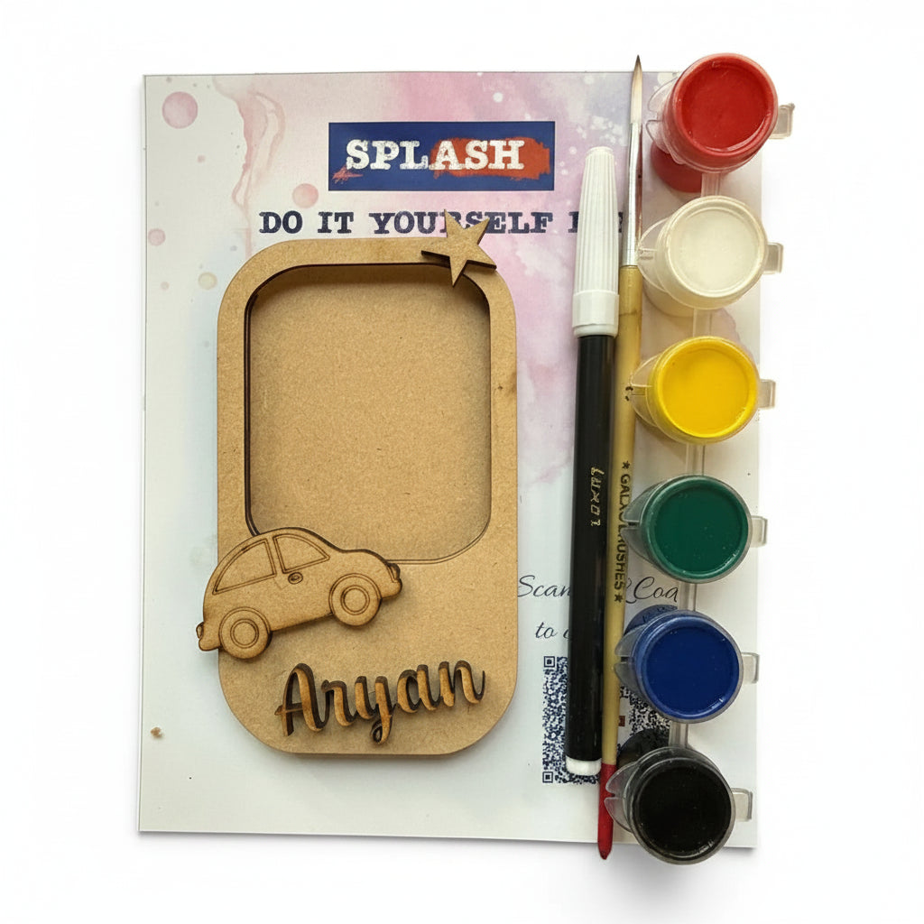 A personalized wooden photo frame kit with a laser-cut wooden car and the name 'Anyan' on a kraft wood base, shown with a paint palette, paint cups, a paintbrush, and a marker on its backing card. The brand 'SPLASH' is visible on the card.