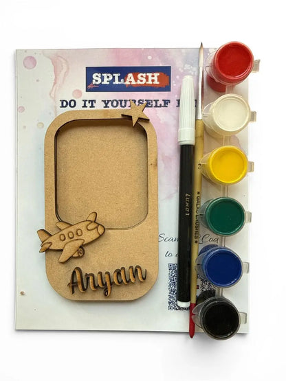 Personalized kids' watercolor painting kit featuring a laser-cut wooden airplane window frame, a paint palette with six color wells, a paintbrush, and a marker on a white background.