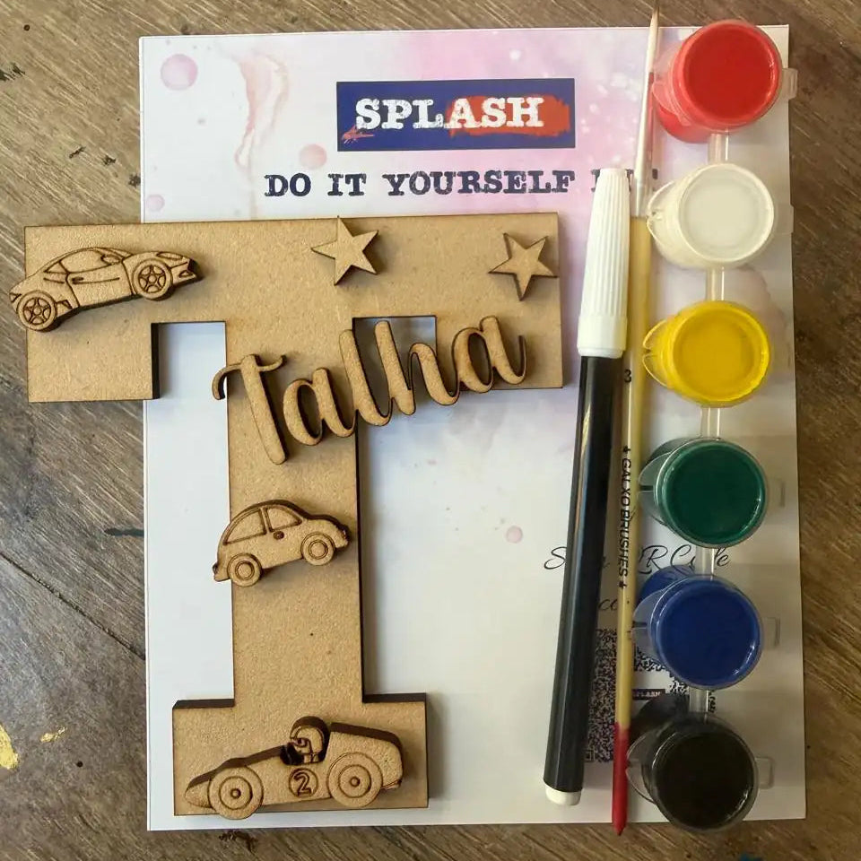 A DIY personalized wooden letter T paint-by-numbers kit for kids, featuring a wooden letter T with laser-cut car and star details, a paint palette with six colors, a paintbrush, and a paint marker on a white instruction sheet over a wooden table.