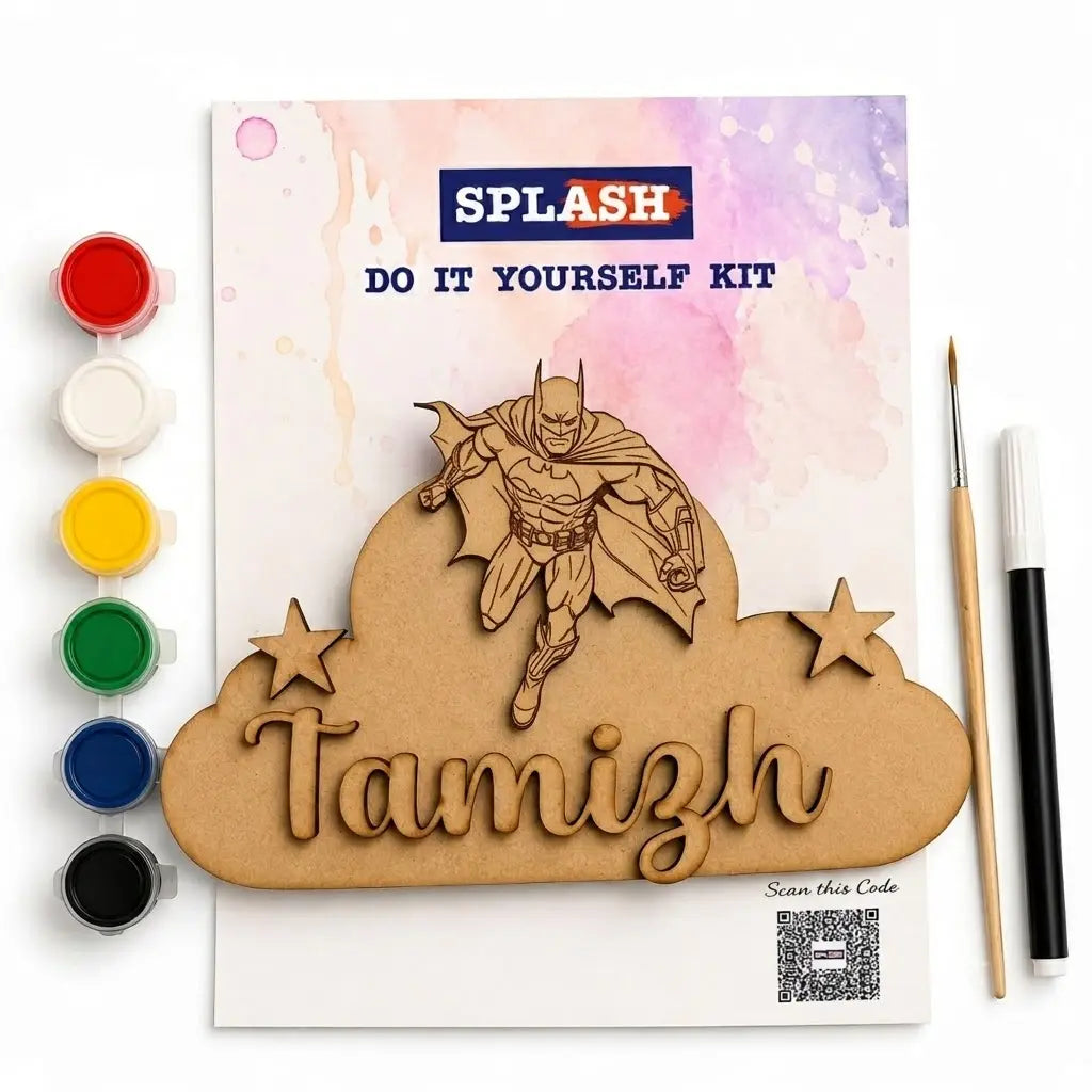 A DIY laser-cut and paint kit shown on a white background, including a printed card with a Batman illustration, a cloud-shaped wooden cutout with the name Tamizh, five paint pots, a fine-tip brush, and a marker pen.