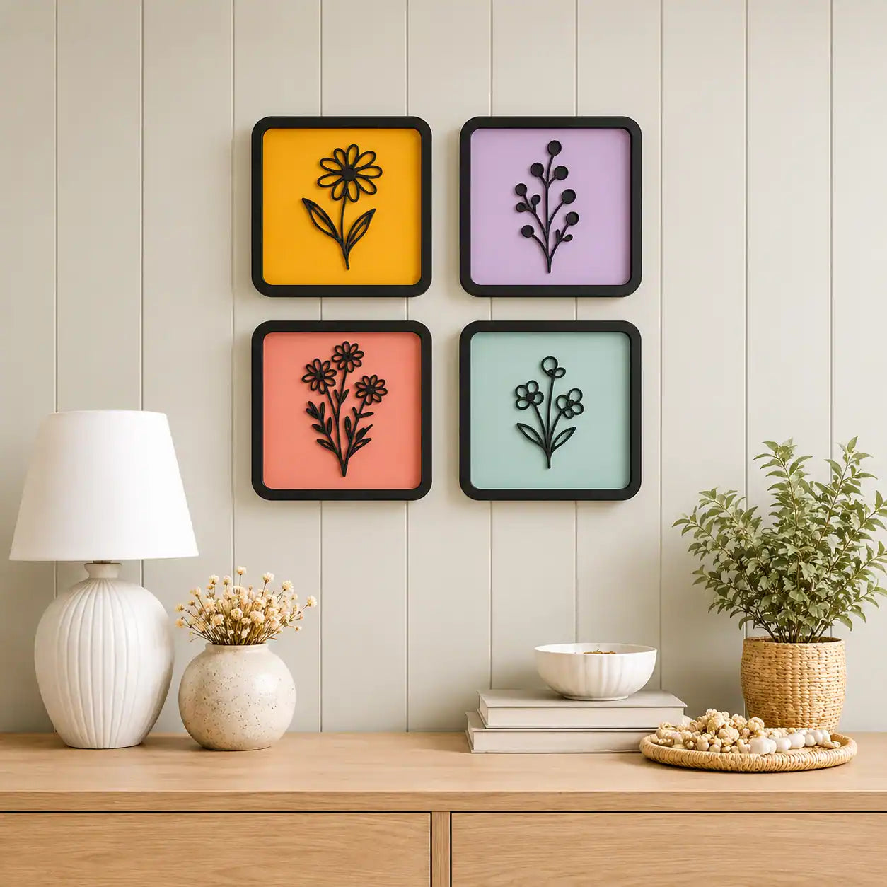 Four colorful wall art pieces with floral designs on a wooden shelf against a light wooden paneled wall.