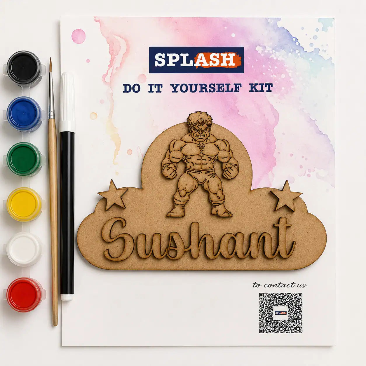A DIY craft kit package shown on a white background with paint pots, a paintbrush, and a wooden nameplate design featuring a muscular cartoon character and the name 'Sushant.' The package text reads 'SPLASH' and 'DO IT YOURSELF KIT.