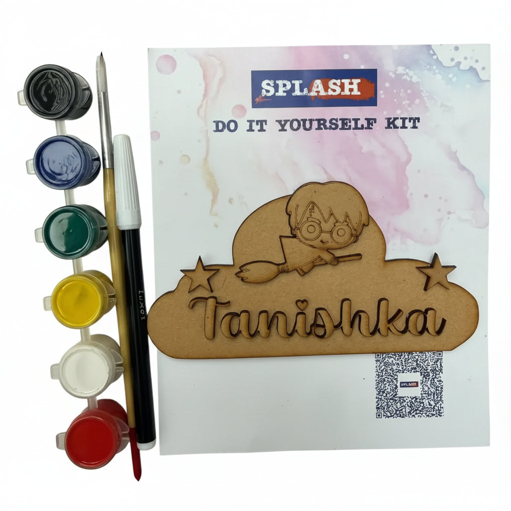 A DIY craft kit labeled 'SPLASH DO IT YOURSELF KIT' with a wooden nameplate reading 'Tanishka' and a cartoon character, shown with paint pots, brushes, and a palette on a textured beige fabric background.