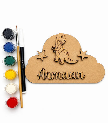 Personalized wooden cloud plaque with a laser-cut dinosaur and the name 'Armaan', shown with a paint palette, paint pots, and a sketch pen on a white background.