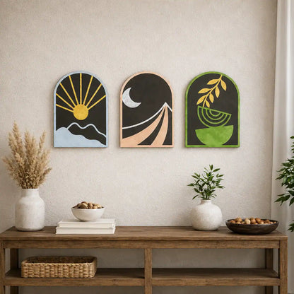 Three decorative wall art pieces above a wooden console table with plants and books.