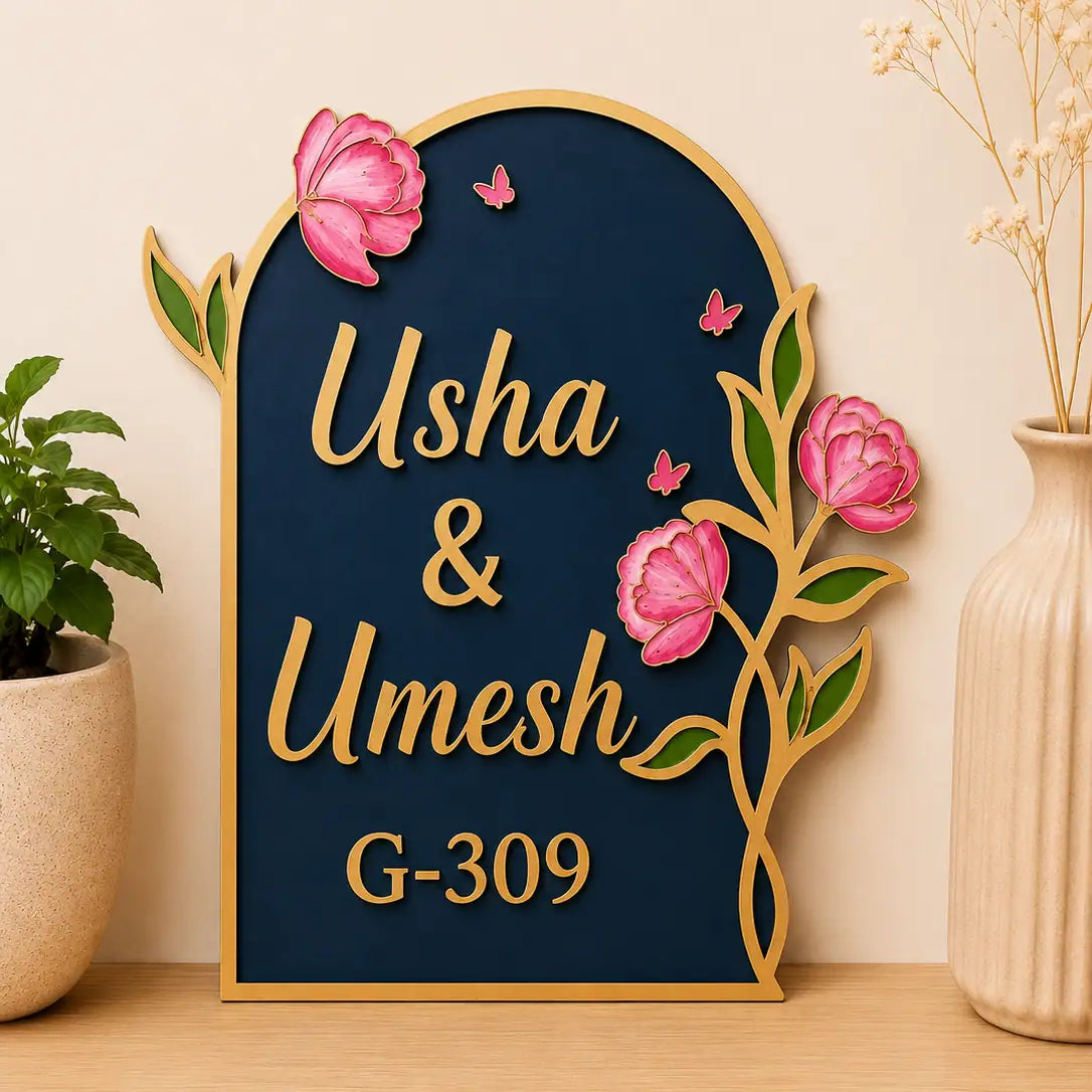 Decorative sign with 'Usha & Umesh' and house number 'G-309' on a blue background with floral designs.